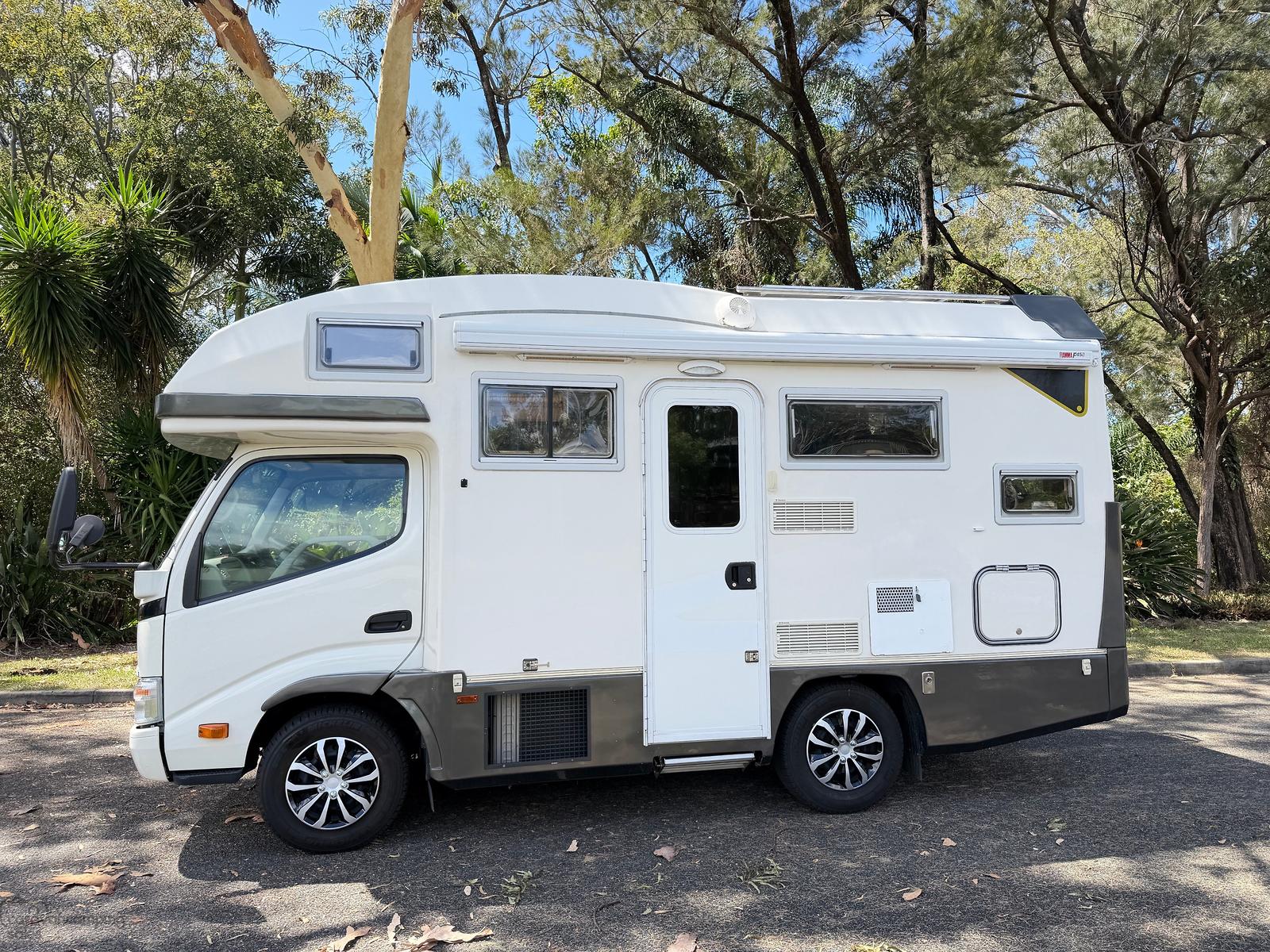 The actual white Toyota Camroad, entrance side, parked beneath trees